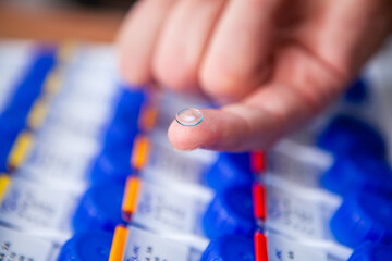 A male optician doctor shows a new clear and clean contact lens resting on a finger. In the...