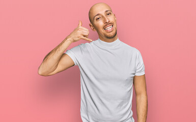 Bald man with beard wearing casual white t shirt smiling doing phone gesture with hand and fingers like talking on the telephone. communicating concepts.