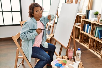 Middle age hispanic woman at art studio painting on canvas with angry face, negative sign showing...