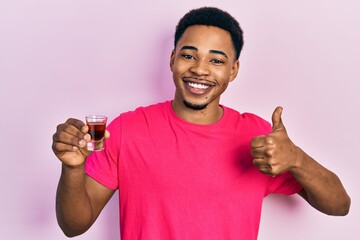 Young african american man drinking whiskey shot smiling happy and positive, thumb up doing...