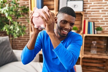 Young african american man holding piggy bank sitting on sofa at home