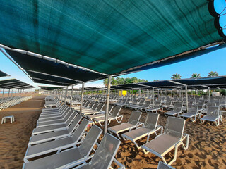 Many empty brown sun beds standing on morning sunny empty sandy beach. Equipment for safe and convenient resting on shore of sea in hotel resort