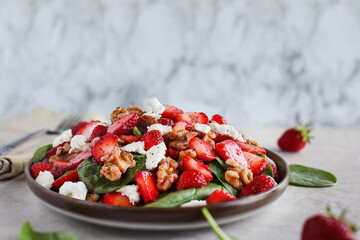 Plate of homemade fresh salad of baby spinach leaves, sliced strawberries, walnuts, feta cheese,...