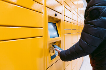 Detail of the arm of a man scanning a code on the mobile phone to pick up a package from the yellow locker. Messaging concept, compare online, e-commerce and packages © Davidbenito