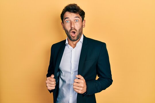 Handsome man with beard wearing business suit holding jacket afraid and shocked with surprise and amazed expression, fear and excited face.