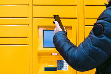Detail of the arm of a man scanning a code on the mobile phone to pick up a package from the yellow...