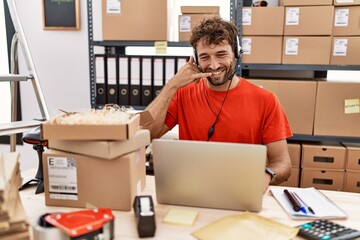 Young hispanic call center agent man working at warehouse smiling doing phone gesture with hand and fingers like talking on the telephone. communicating concepts.