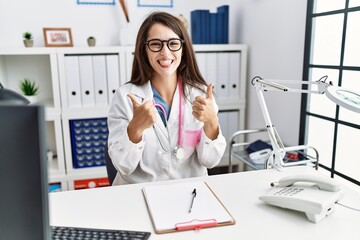 Obraz na płótnie Canvas Young doctor woman wearing doctor uniform and stethoscope at the clinic success sign doing positive gesture with hand, thumbs up smiling and happy. cheerful expression and winner gesture.