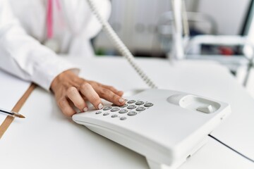 Fototapeta premium Young hispanic woman wearing doctor uniform talking on the telephone at clinic