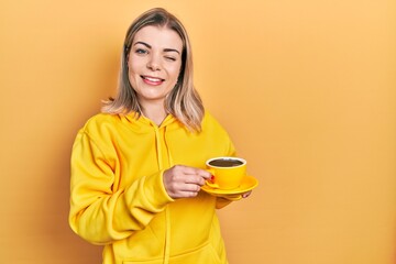 Beautiful caucasian woman drinking a cup coffee winking looking at the camera with sexy expression,...