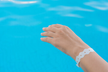 Closeup view stock photography of one empty female hand isolated on blurry blue pool water background. Wrist with white wristband bracelet 