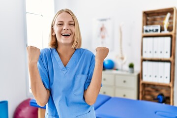 Obraz premium Young caucasian physiotherapist woman working at pain recovery clinic screaming proud, celebrating victory and success very excited with raised arms