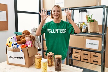 Young caucasian woman wearing volunteer t shirt at donations stand showing and pointing up with...