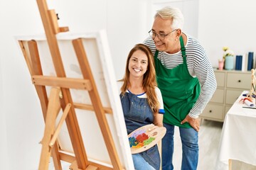 Two middle age artists smiling happy painting at art studio.