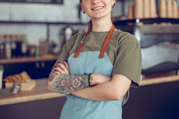 Cheerful female barista in apron standing in coffee shop