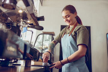 Cheerful woman barista making coffee in cafeteria - obrazy, fototapety, plakaty