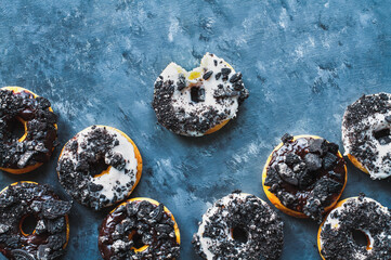 Flatlay of dark and white chocolate frosted donuts with crumbled creme filled cookies over a blue textured painted background.