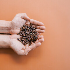 Close up of roast coffee beans in hand on brown background with copy space