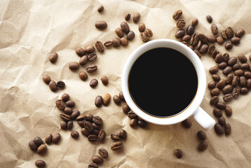 Flat lay view of black coffee cup on crumple brown paper with coffee beans