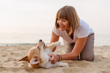 Senior woman smiling while resting with her dog on beach