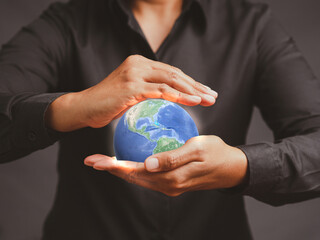 Young man holding the earth while standing against a gray background.