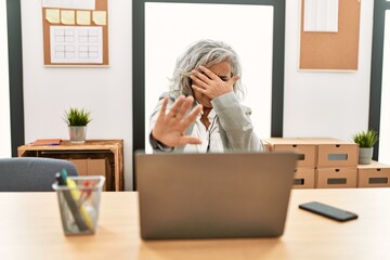 Middle age businesswoman sitting on desk working using laptop at office covering eyes with hands and doing stop gesture with sad and fear expression. embarrassed and negative concept.