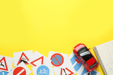 Many different road sign cards, notebook and toy car on yellow background, flat lay with space for...