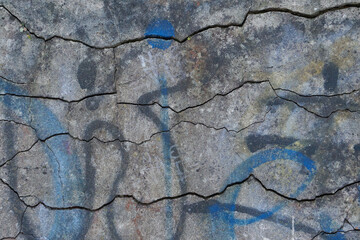 Old cracked concrete wall with multicolored paint and graffiti. Close-up view of rough beton surface with cracks. Abstract wallpaper, texture or background