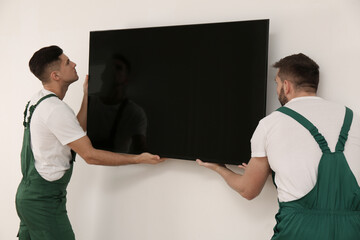 Professional technicians installing modern flat screen TV on wall indoors