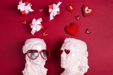 White female and male plaster heads with heart shaped glasses, hearts and gifts overhead on red background.