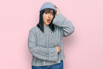 Young hispanic woman wearing cute wool cap surprised with hand on head for mistake, remember error....