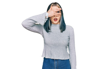 Fototapeta premium Young modern girl wearing casual sweater peeking in shock covering face and eyes with hand, looking through fingers with embarrassed expression.