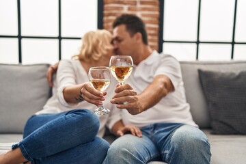 Middle age man and woman kissing and hugging each other toasting with champagne at home