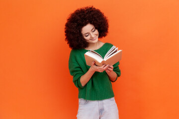 Happy smiling woman with Afro hairstyle wearing green casual style sweater reading book with...