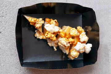 cheesecake with salted caramel and popcorn in a black paper packaging box for delivery on a gray background, close-up.