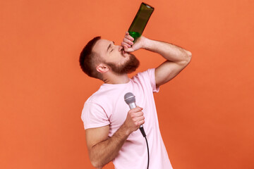 Portrait of drunk bearded man spending time in karaoke, holding microphone in hand, drinking...