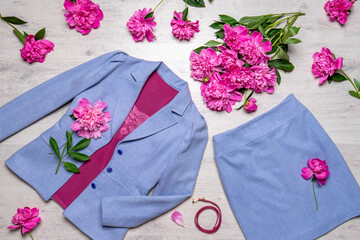 Women classic suit in lavender color with pink accessories and peonies on light background. Jacket and skirt with blouse and belt. Spring flowers. Beautiful stylish clothes, fashionable outfit