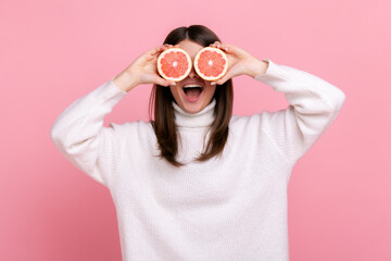 Positive woman covering eyes with two half slices of grapefruit, detox and healthy raw fresh food,...