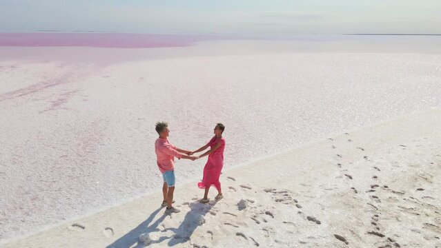 Aerial epic drone image of lovely romantic couple walking along bright colorful pink water of mineral lake with white salty coast. panoramic view. Concept inner tourism in unusual places in Ukraine
