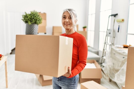 Middle age grey-haired woman smiling confident holding package at new home