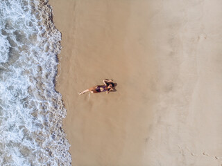 Young pretty lovely woman in a bikini lying on the back on the white sand near the waves of blue sea. Top view.