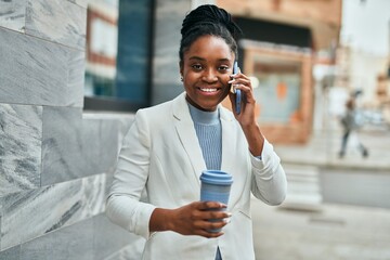 Young african american businesswoman talking on the smartphone and drinking coffee at the city.