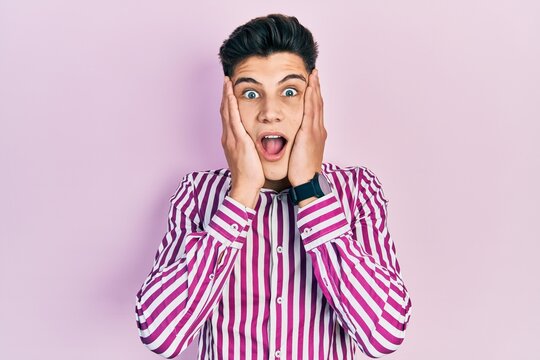 Young hispanic man wearing casual clothes afraid and shocked, surprise and amazed expression with hands on face