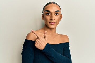 Obraz premium Hispanic man wearing make up and long hair wearing woman fashion clothes smiling cheerful pointing with hand and finger up to the side
