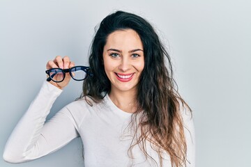 Young hispanic woman holding glasses looking positive and happy standing and smiling with a confident smile showing teeth