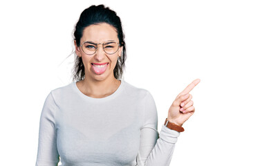 Young hispanic woman pointing with fingers to the side sticking tongue out happy with funny...