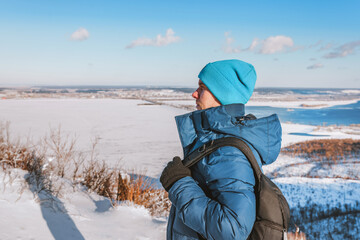 A young man stands on a high mountain with a beautiful winter snowy landscape on a sunny day