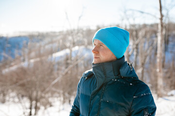 Portrait of a young man in a blue hat in a snowy winter forest in sunlight