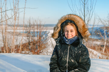 Cute little girl in a warm jacket in a snowy forest on the background of a winter landscape on a high mountain