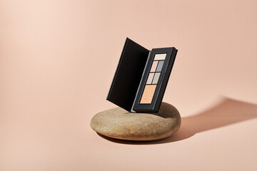 Pastel  eyeshadows kit in a black paper case on a river pebble stones on a beige background